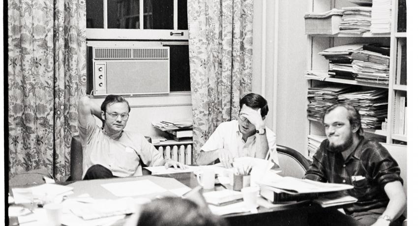 Black and white photograph of three men sitting at a table in an office.